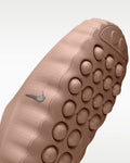 Close-up of the textured outsole of a Nike shoe in a dusty rose or mauve color, featuring a silver Nike Swoosh and circular tread patterns, set against a light gray gradient background.