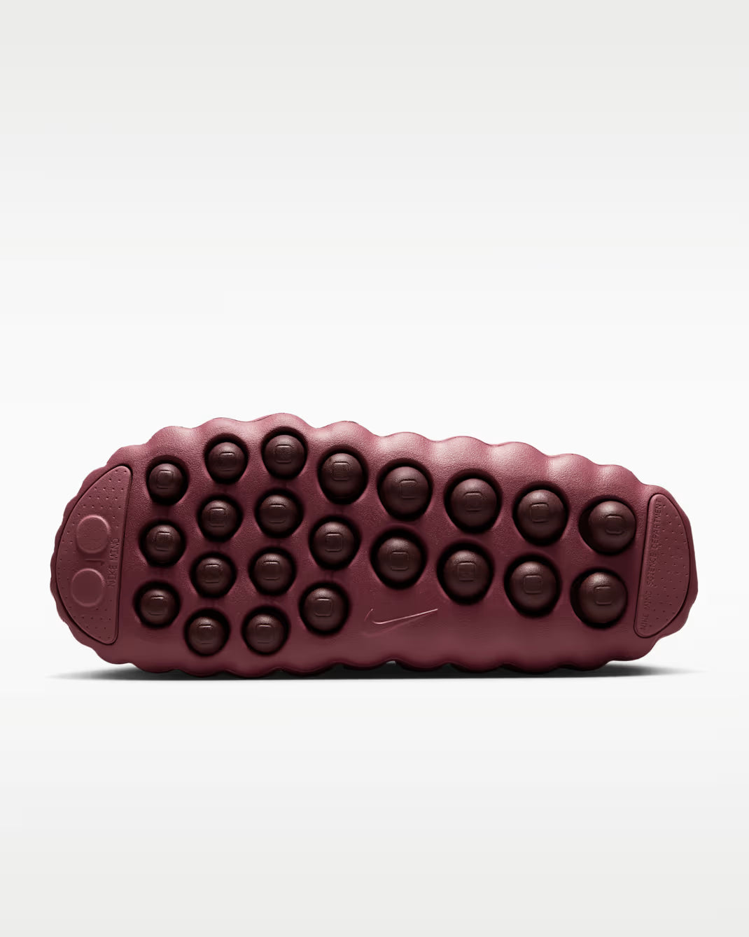 The textured outsole of a Nike shoe in a deep burgundy color, featuring rows of circular raised nubs and a small embossed Swoosh logo, shown against a light gray background.